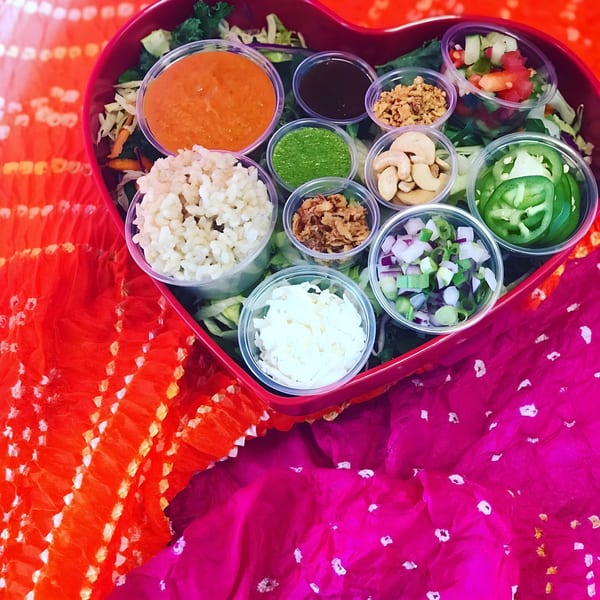 Heart-shaped bowl filled with healthy ingredients like rice, cashews, sauces, and vegetables.