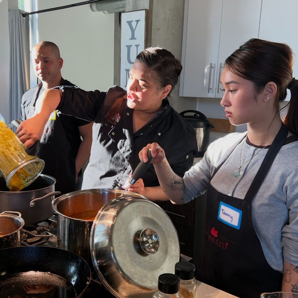 Three restaurant staff members prepare food in large pots and pans in a bright commercial kitchen.