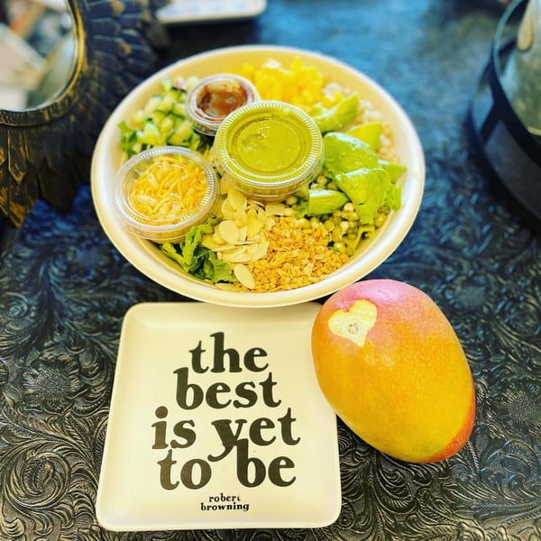Eats Meets West Bowls' healthy bowl with avocado, nuts, and sauces, next to a mango and a decorative plate.