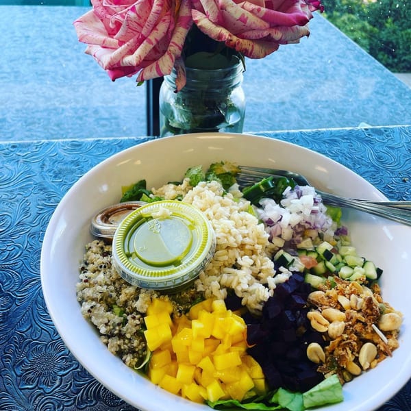 A colorful Eats Meets West Bowl with quinoa, mango, beets, and peanuts, next to a pink rose.
