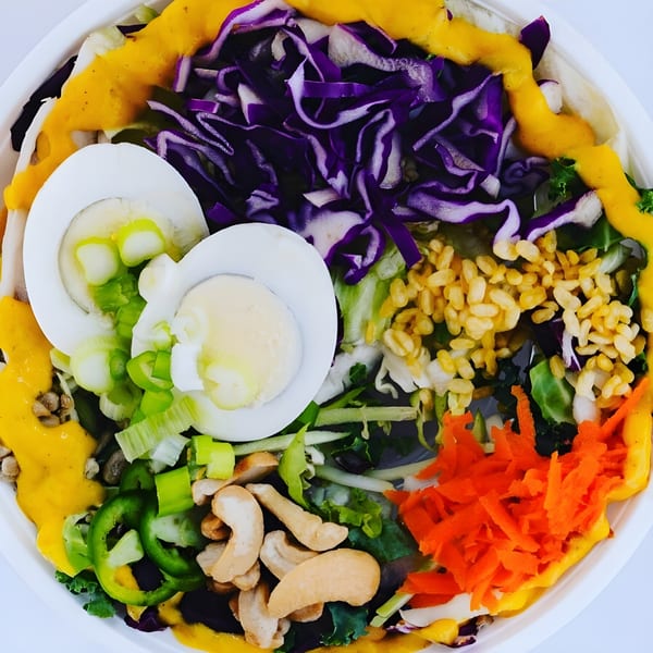 Colorful Eats Meets West Bowl with eggs, purple cabbage, carrots, cashews, and yellow dressing.